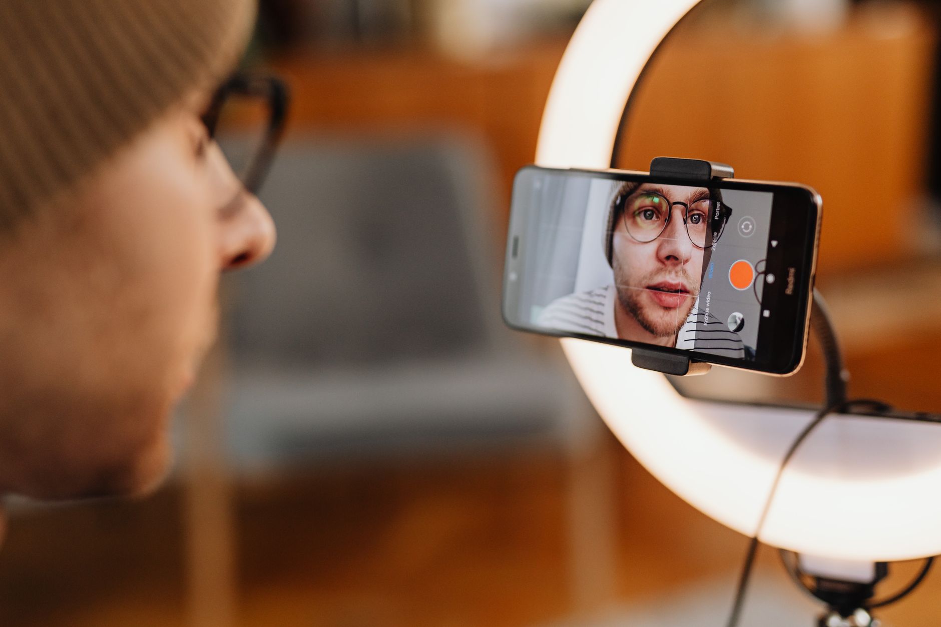 Gros plan sur une personne qui filme une vidéo avec son smartphone et un anneau lumineux, à l'intérieur.